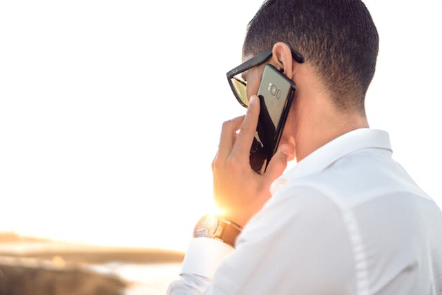 Person wearing glasses, holding a phone up to their ear